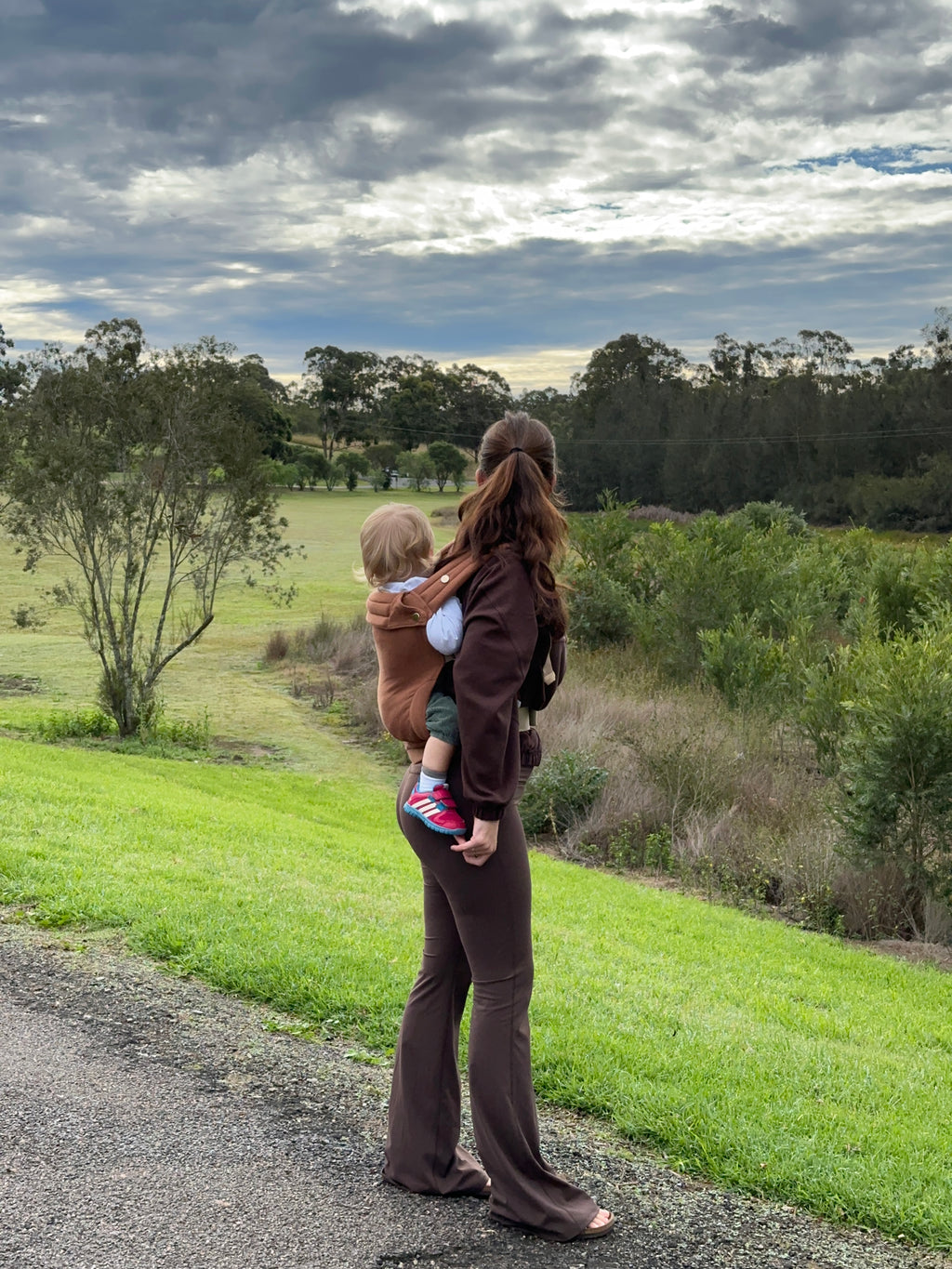 Clay | Mum carrying baby in August baby carrier outside in nature on gravel path with tree's