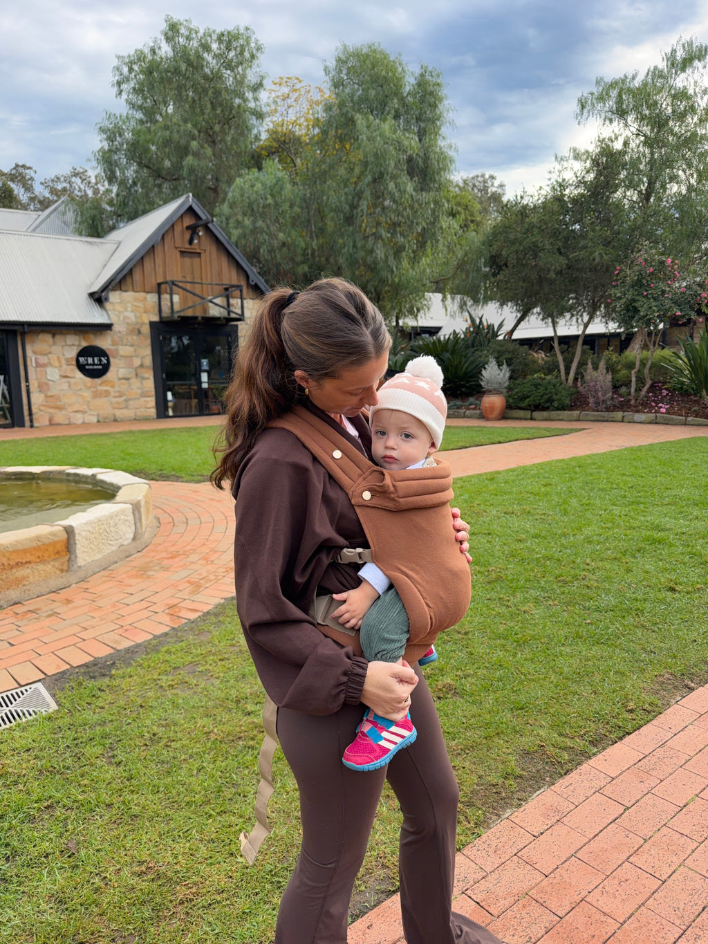 Clay | Mum carrying baby in August baby carrier outside in front of cafe side view