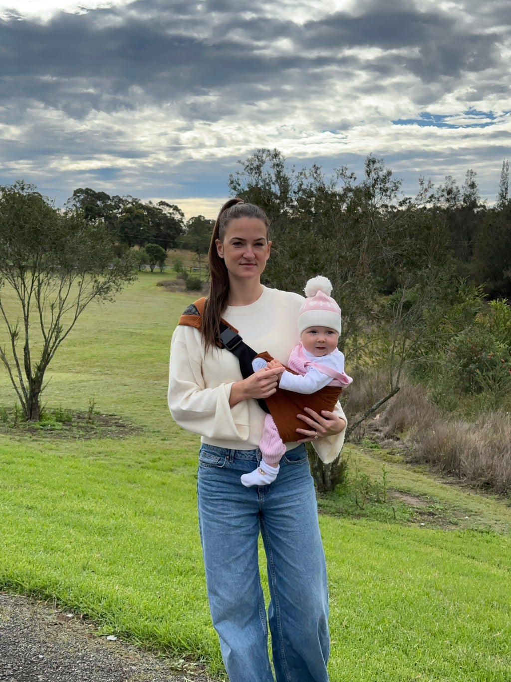 Rust | Woman holding a baby in ever carrier in a field with a lake in the background